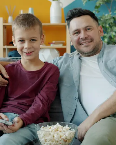Pappa och son skrattar i soffan med en skål popcorn