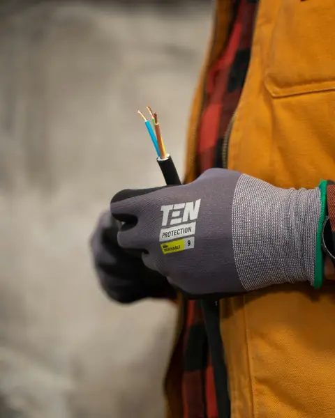 Elektriker i arbetshandskar håller en avskalad elkabel