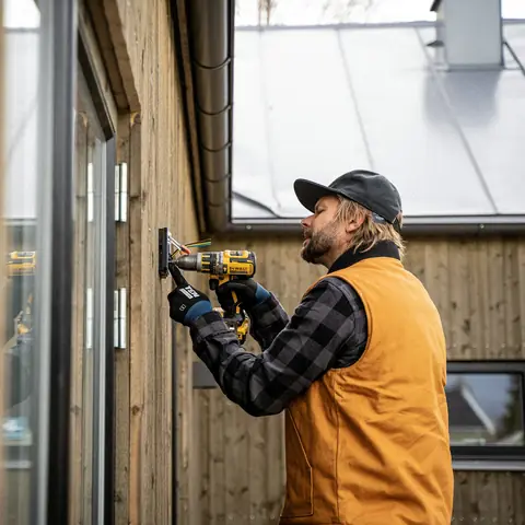 Elektriker med keps drar in el på fasaden till ett trähus