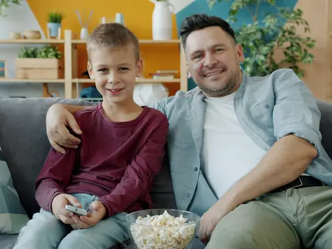 Pappa och son i soffan med popcorn